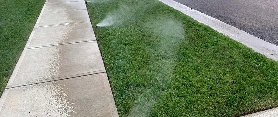 Sprinkler irrigation system watering grass by a sidewalk in Harrisburg, SD.
