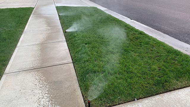 Sprinklers watering a lawn by a sidewalk in Harrisburg, SD.